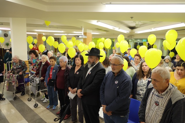 הבית הספרדי ערך אירוע מרגש במיוחד – לזכר הנופלים ולמען השבת החטופים דיירי הבית הפריחו לאוויר בלונים צהובים ורבים מהם דמעו לאורך הטקס ∙ מנכ"לית הבית הספרדי, נטעלי בן: "אף אחד מאיתנו לא נשאר אותו בן אדם מה-7/10" ∙ עו"ד יוסי גילאור, יו"ר ועד העדה הספרדית: "כולנו מייחלים לפתרון שישיב אלינו במהרה את כל החטופים כולם" עם ישראל כולו ניצב מאוחד לצד משפחות החטופים, ומחבק את משפחות הנופלים במערכה הקשה. בבית הספרדי נערך טקס מיוחד, שהביא לידי ביטוי את מכלול הרגשות של הנהלת הבית, העובדים והדיירים – ואת הרצון לתמוך במשפחות. באירוע לקחו חלק חברי ועד העדה היהודית ספרדית, הנהלת הבית, דיירים, עובדים ואורחים. "מה-7/10 אני חושבת שאף אחד מאיתנו לא נשאר אותו בן אדם", ביטאה נטעלי בן, מנכ"לית הבית הספרדי, את מה שכולנו מרגישים. נטעלי ציינה שגם הבית הספרדי כארגון השתנה, והחמיאה לתרומת ועד העדה למאמץ המלחמתי ולחיזוק העורף. סמנכ"ל הבית הספרדי, עדי מתתיהו, העביר מסר של חיזוק ושותפות למשפחות המתמודדות עם מציאות בלתי נתפשת, וביקש "לשדר אנרגיה טובה ליקום כדי שמשהו טוב יקרה כבר". גם עו"ד יוסי גילאור, יו"ר ועד העדה הביע תקווה: "כולנו מתפללים ומייחלים שנתבשר במהרה על פתרון שישיב אלינו את כל החטופים כולם". דיירי הבית ענדו כפתורים ועליהם הקריאה "מחזירים אותם הביתה, עכשיו!". רבים מהם דמעו לאורך הטקס, וניכר היה שכל הנוכחים מתרגשים מאוד. רב הבית הספרדי נשא תפילה, ובסיום האירוע הופרחו לאוויר בלונים צהובים, שמסמלים את התפילה של כולנו להחזרה מידית של החטופים.