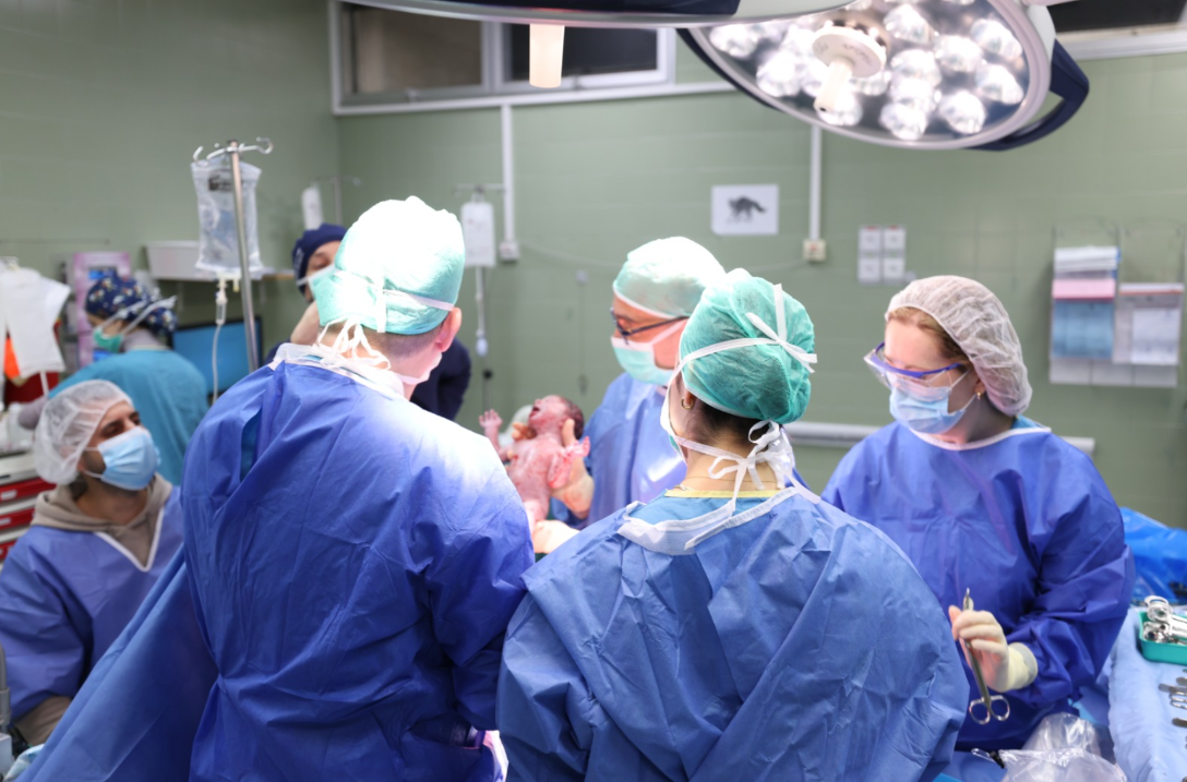 בתמונה: דר ציפורי עם אחד התאומים בחדר הניתוח. בתמונה: מתוך הניתוח הקיסרי שנערך במתחם התת קרקעי הממוגן ברמב"ם. צילום: הקריה הרפואית רמב"ם.